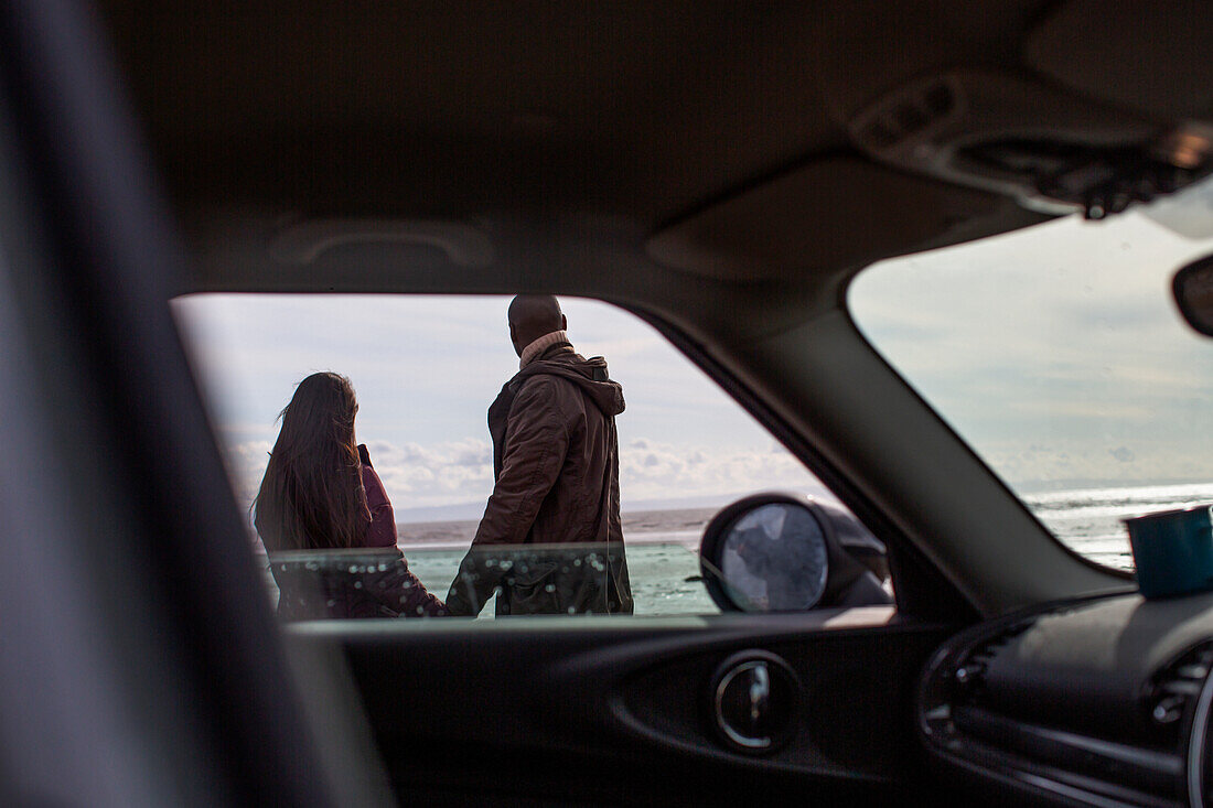 Couple holding hands outside car on winter beach