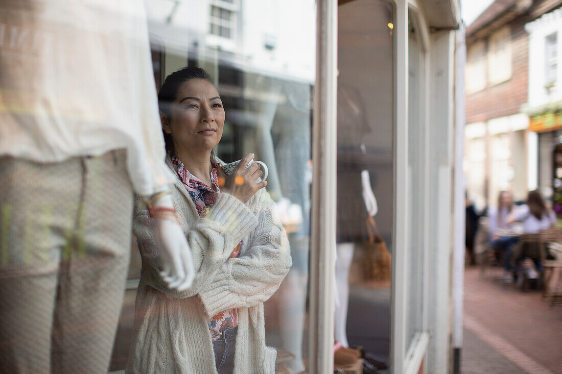 Female shop owner with tea looking out shop window