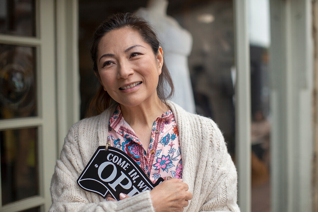 Smiling female shop owner holding open sign