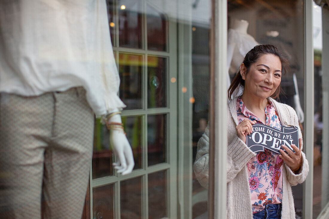 Happy female shop owner with open sign outside boutique