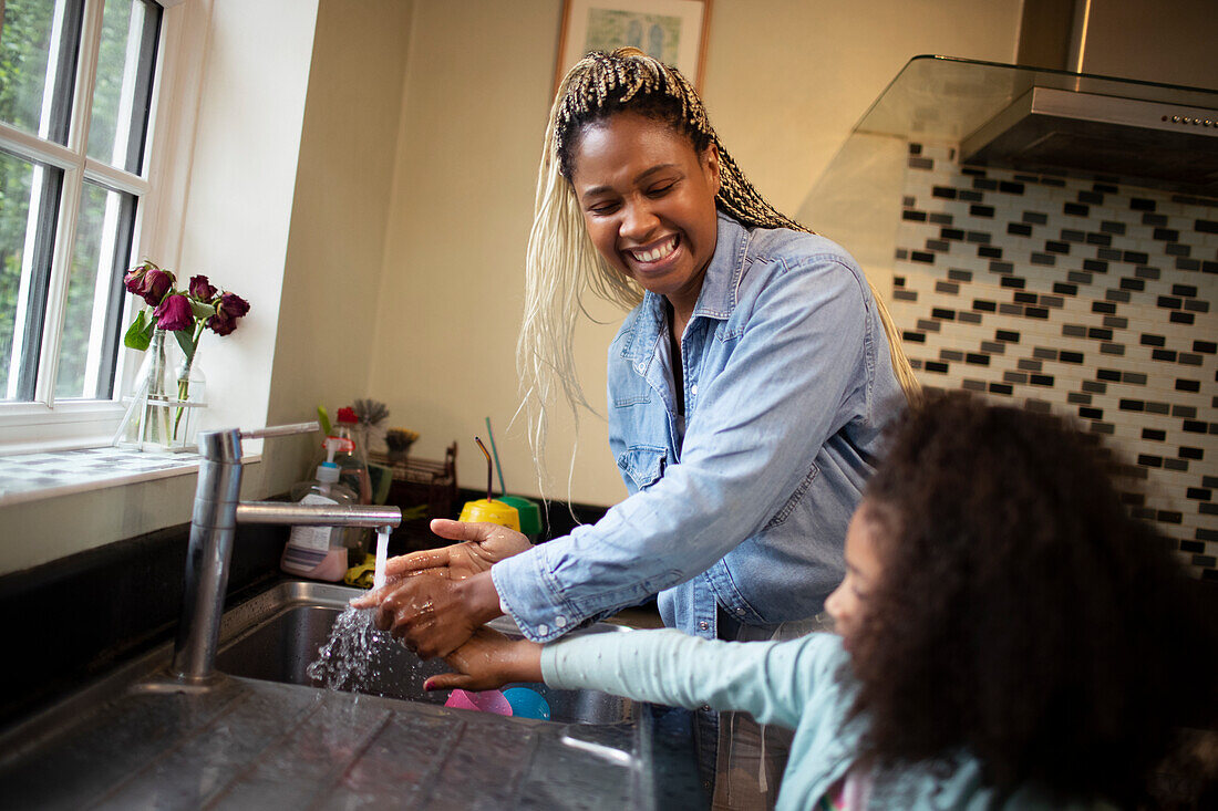 Happy mother helping daughter wash hands at kitchen sink