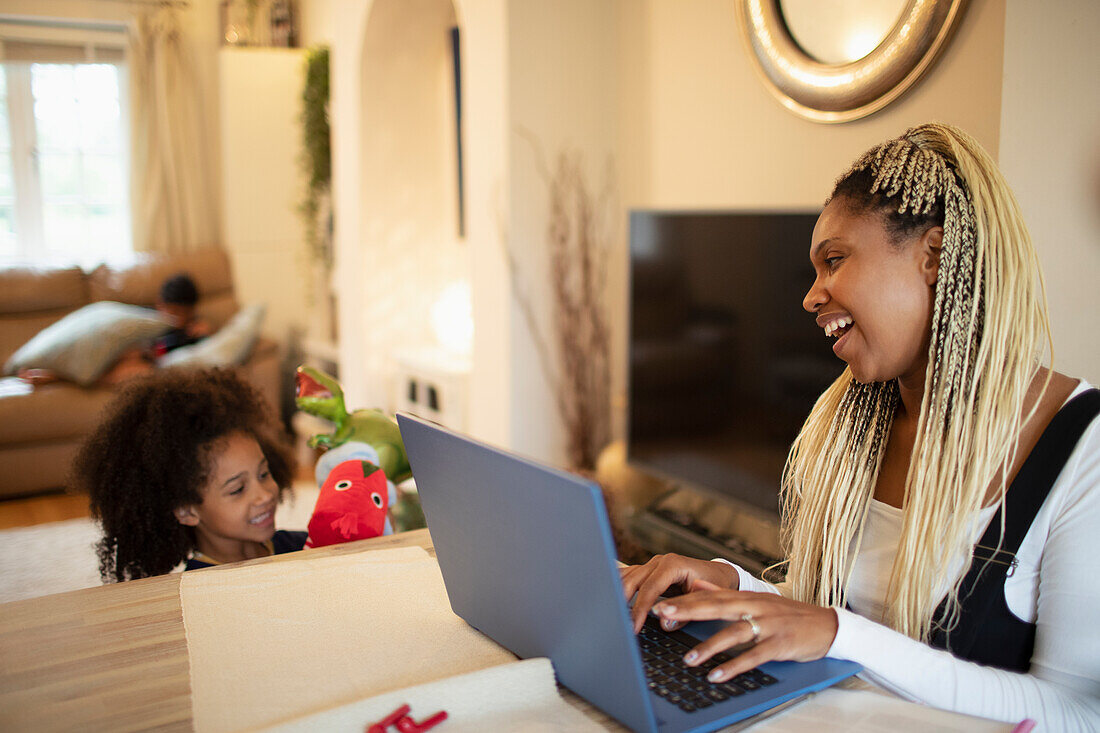 Happy mother working at laptop and watching daughter play