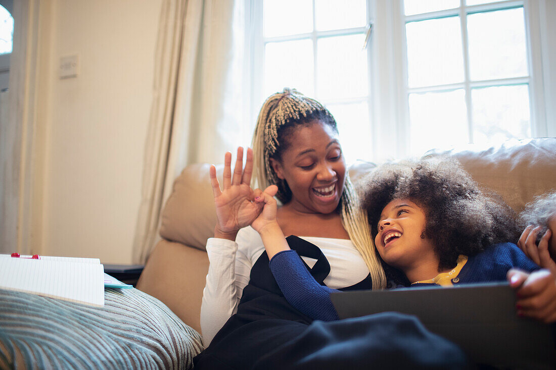 Mother and daughter with digital tablet on living room sofa