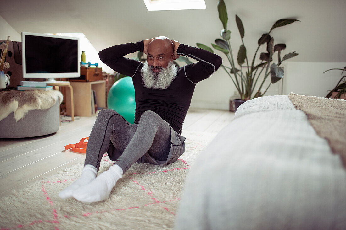 Mature man with beard doing sit-ups on bedroom floor