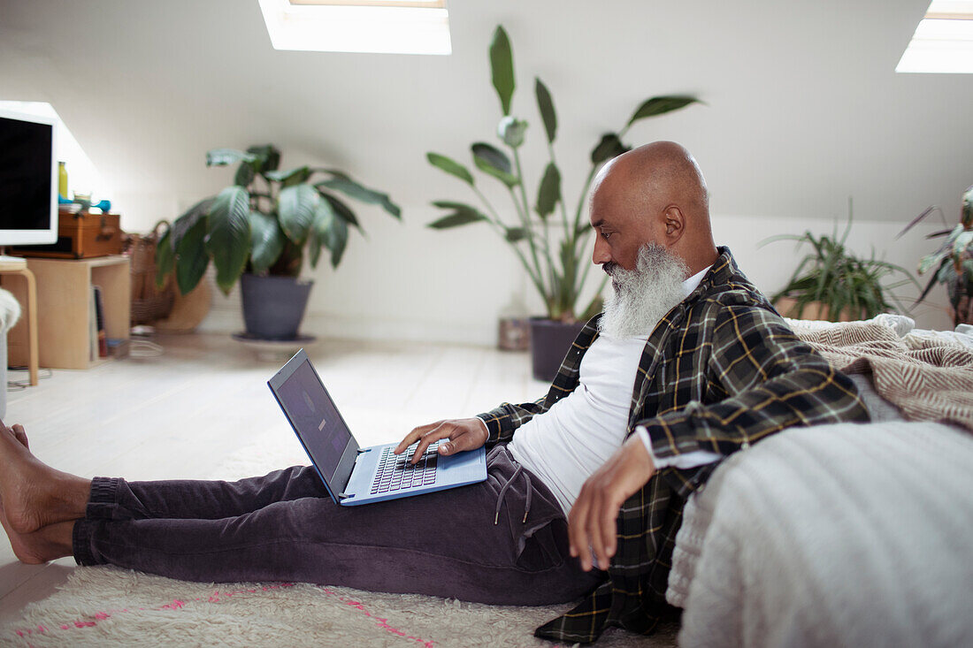 Mature man with beard using laptop on bedroom floor