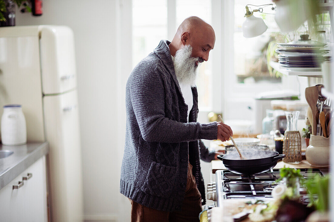 Mature man with beard cooking at kitchen stove