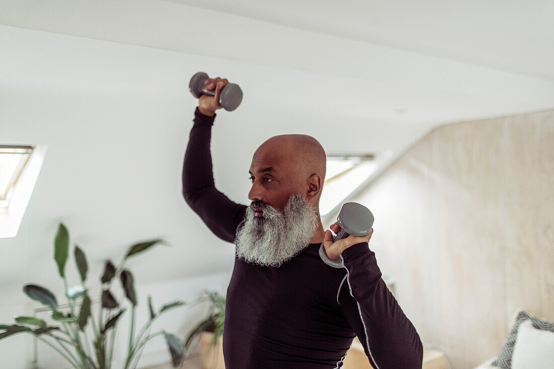 Mature man with beard exercising with dumbbells at home