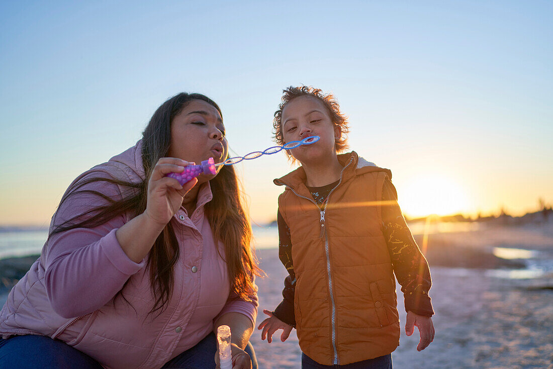 Mother and son with Down Syndrome blowing bubbles on beach