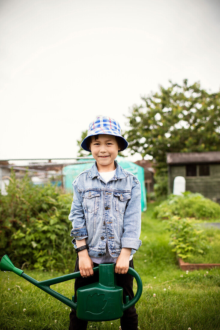 Smiling boy with watering can in vegetable garden