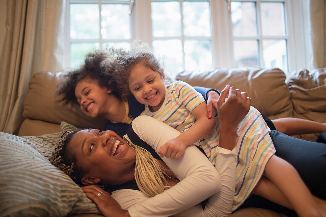 Happy playful mother and daughters on living room sofa