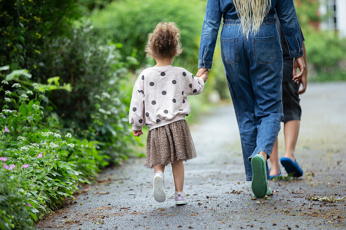 Mother and daughter holding hands walking on driveway