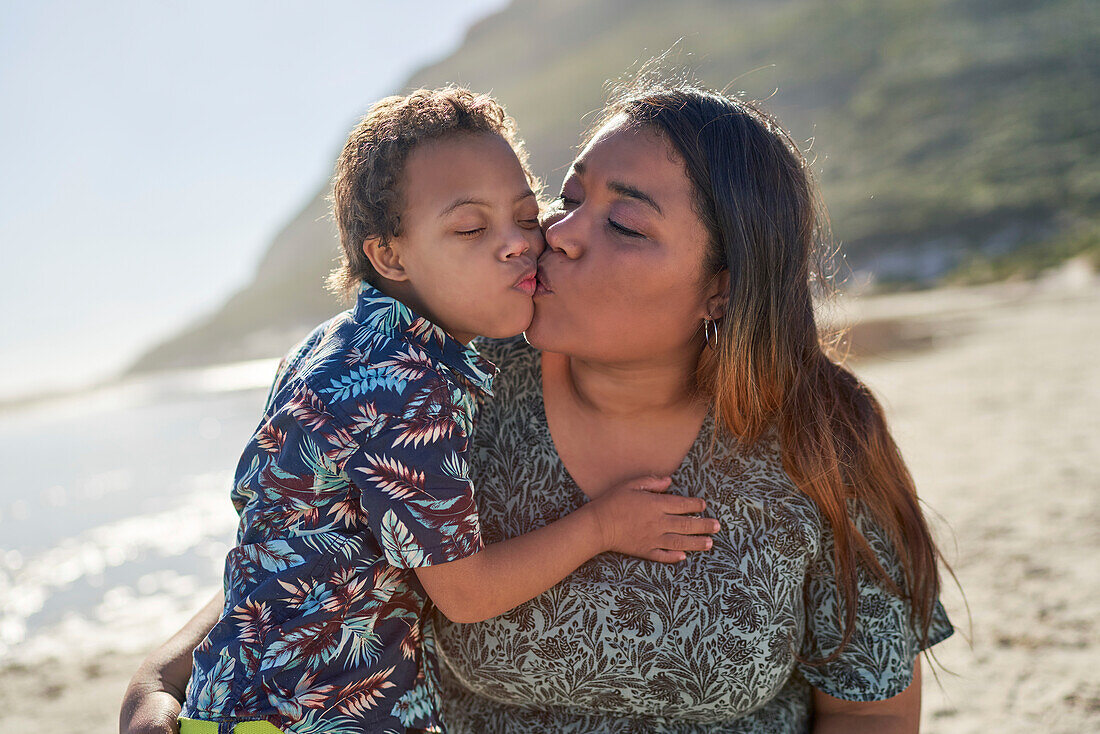 Happy, affectionate mother and son kissing on sunny beach