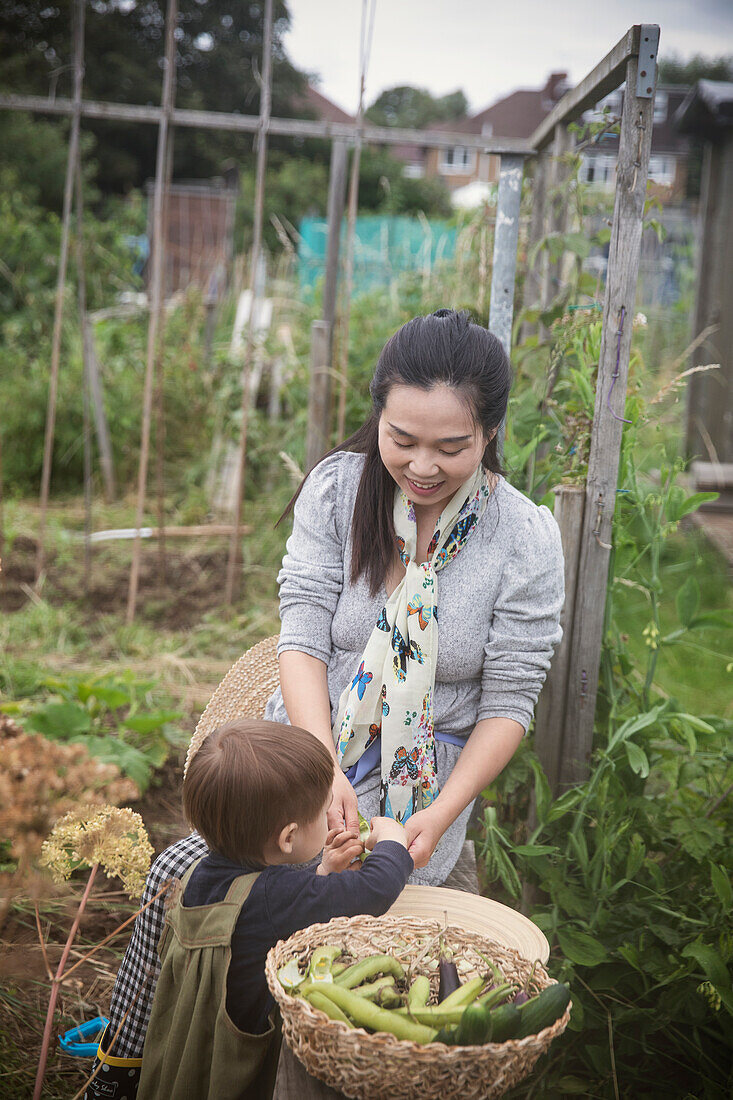 Mother and toddler son with harvested vegetables in garden