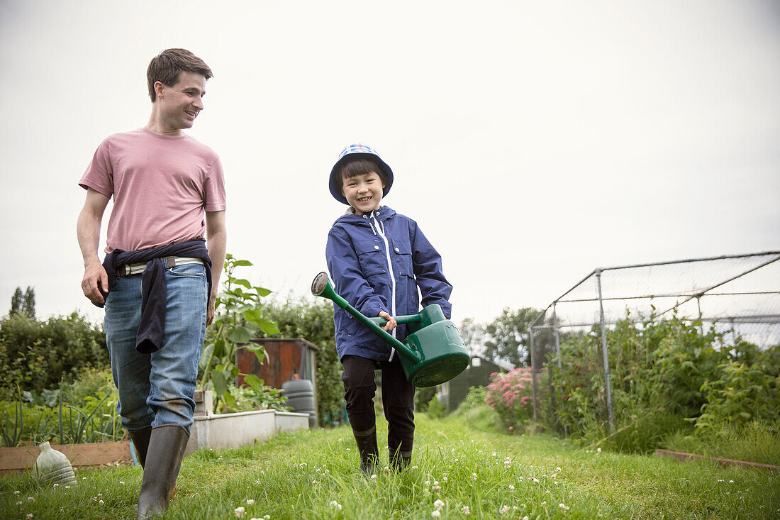 Father and son with watering can walking in garden