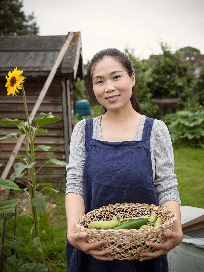 Smiling woman holding basket of harvested vegetables
