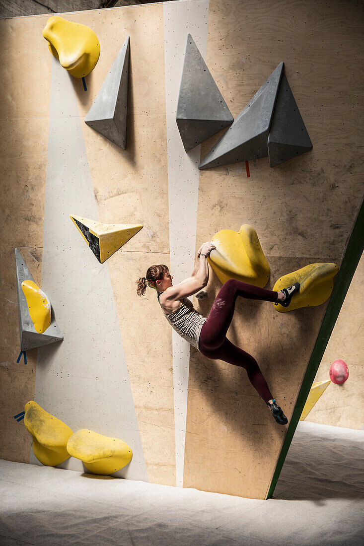 Young female rock climber hanging from climbing wall