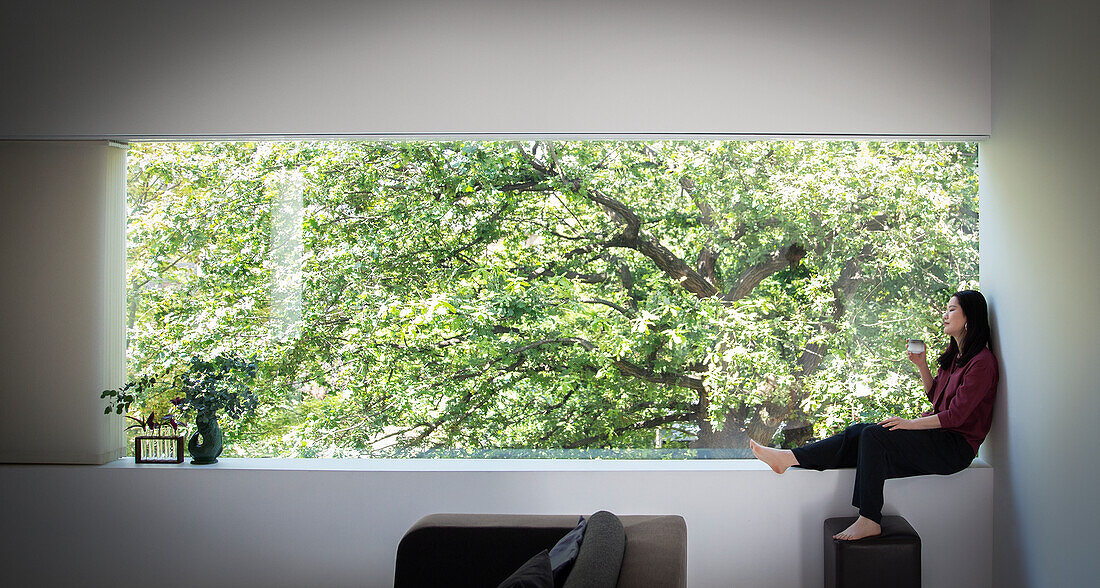 Young woman drinking tea in window with view of tree