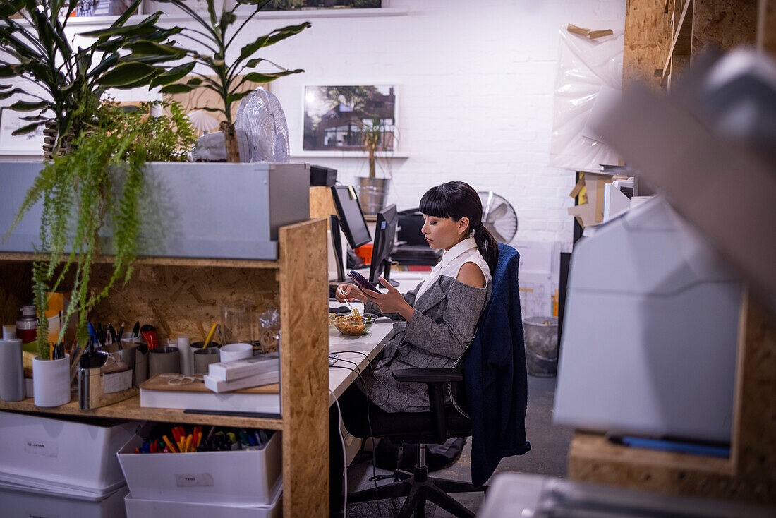 Businesswoman using smart phone at desk in creative office