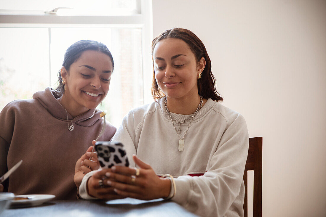 Smiling young adult sisters using smart phone at home