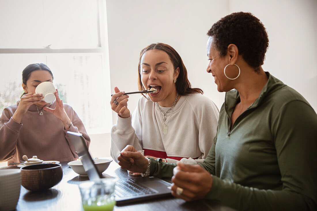 Mother and young adult daughters eating at laptop