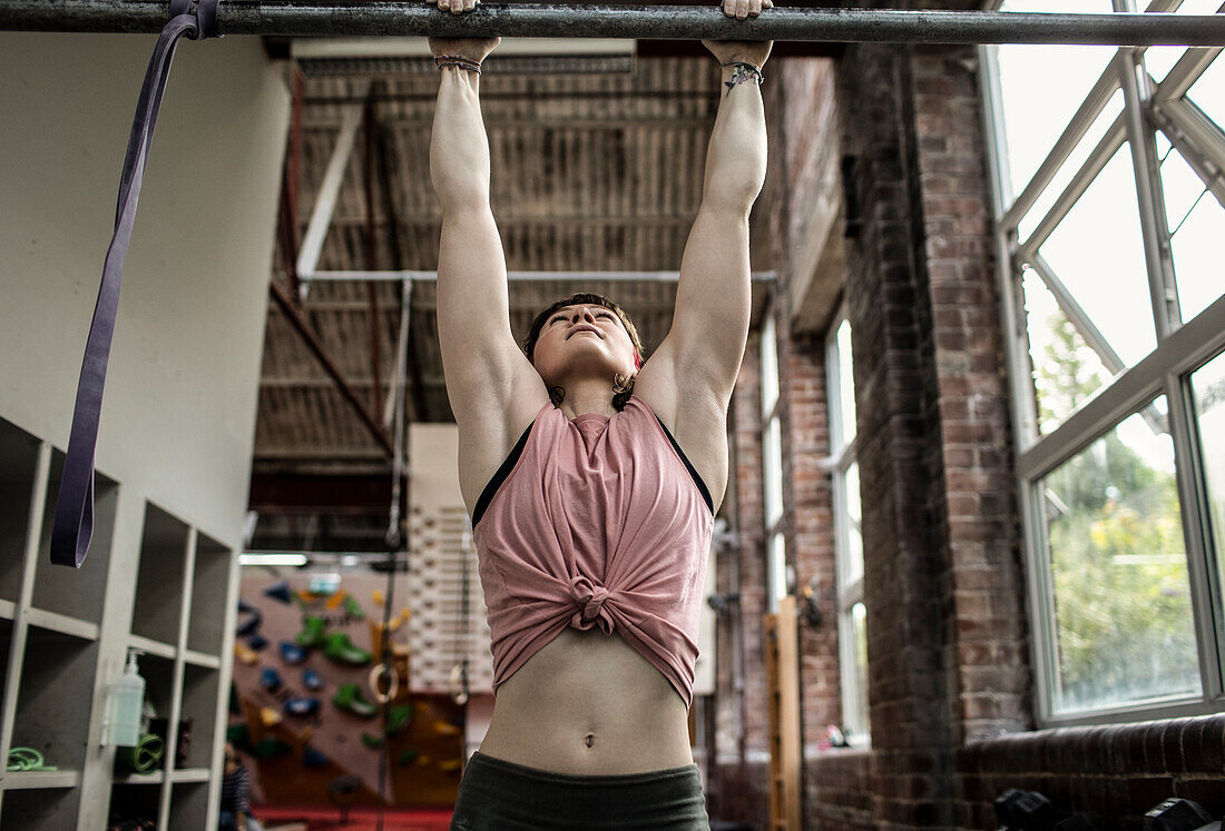 Strong young woman hanging from bar in climbing center