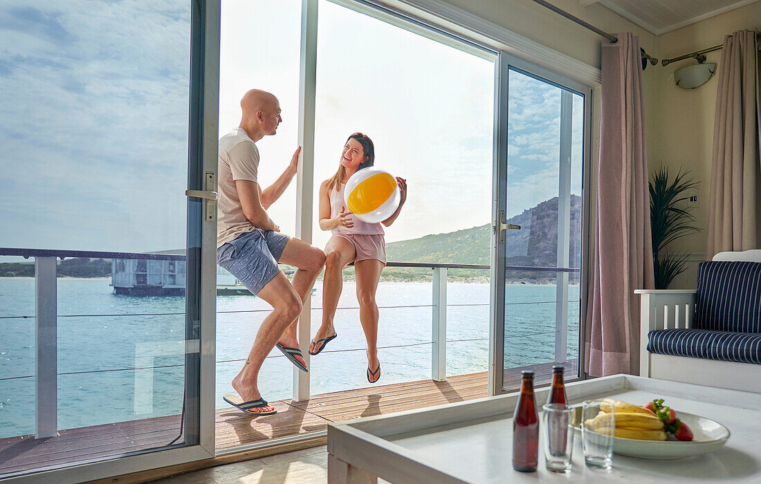 Happy couple with beach ball on houseboat patio on sunny lake