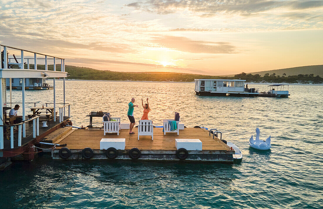 Carefree couple dancing on houseboat patio on lake at sunset