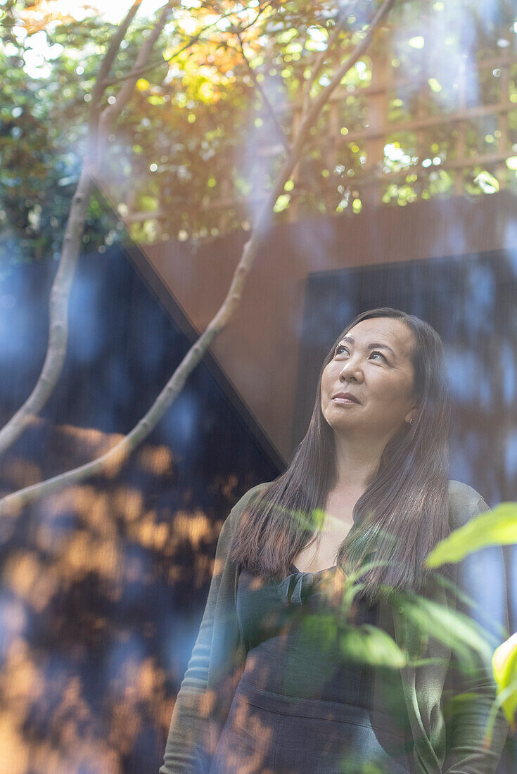 Thoughtful mature woman looking up at tree in courtyard