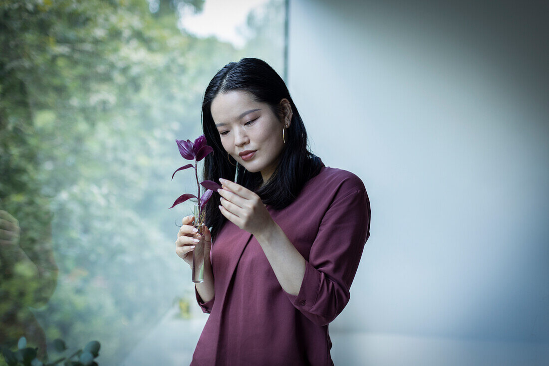 Young woman looking at plant leaf in window