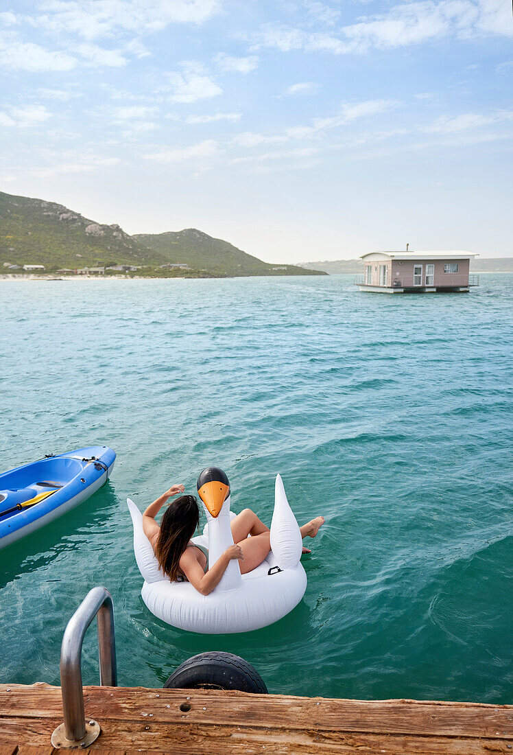 Woman relaxing on inflatable swan in blue ocean