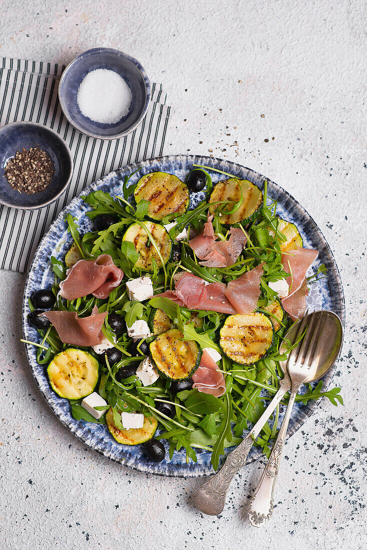 Rocket salad with grilled zucchini, Parma ham, black olives, and feta