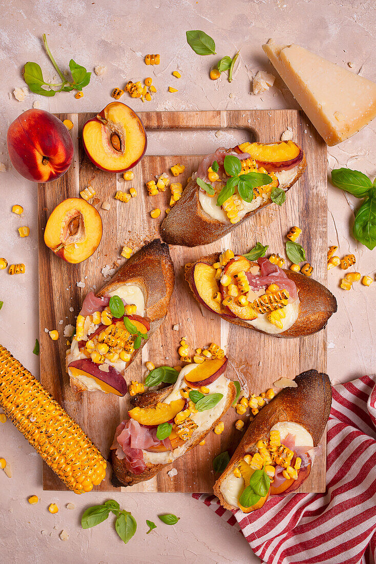 Crostini mit Mozzarella, Pfirsichen, Parmaschinken, Mais, Parmesan und Basilikum