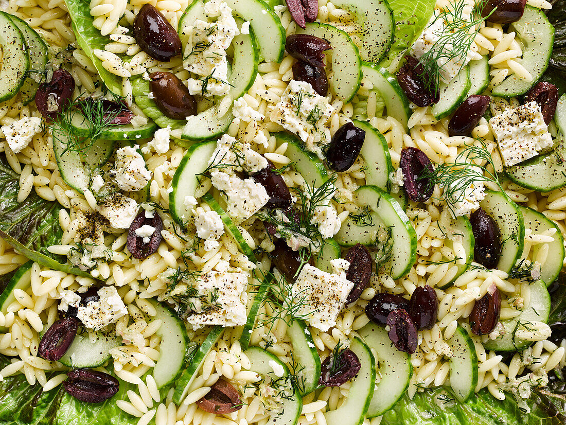 Zitroniger griechischer Orzo-Salat mit Gurke und schwarzen Oliven (bildfüllend)