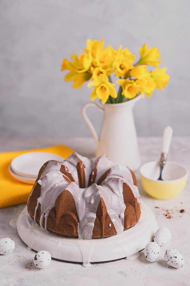 Mandelkuchen mit Zuckerguss zu Ostern dahinter Narzissen in Krugvase