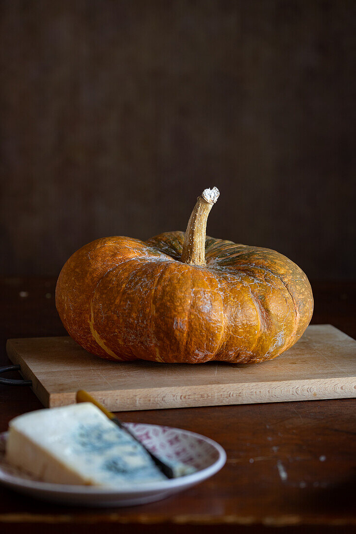 A pumpkin, in the foreground a piece of blue cheese on plate