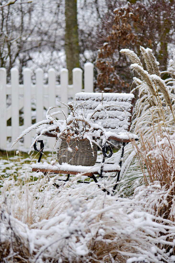 Basket with larch branches on a snowed-in garden chair