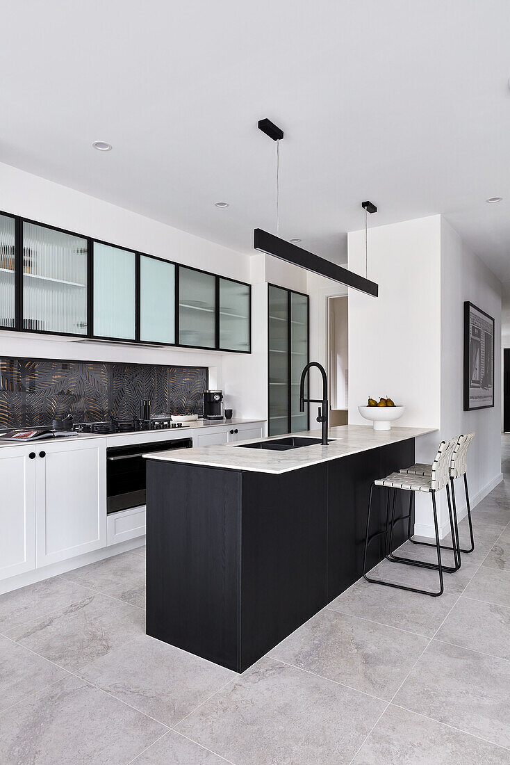 A modern monochromatic kitchen with a thin marble benchtop, black fitting and glass fronted cabinets