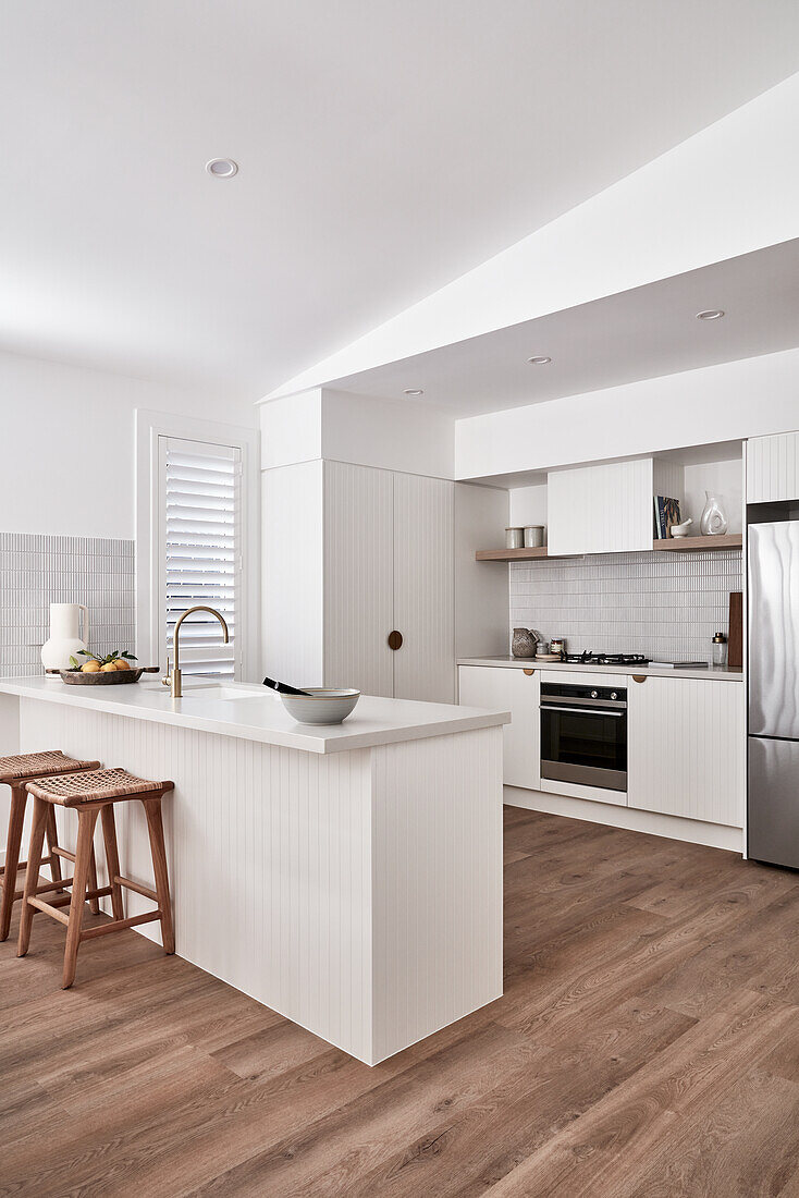 An open-plan kitchen with V-grooved panelling, golden fittings, white woodwork and oak wood flooring, and a living room in a modern Scandi-stlye with plantation shutters