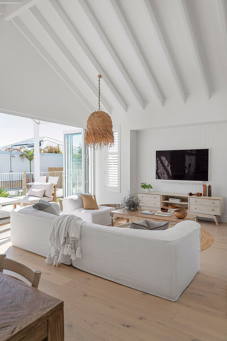 Seating area with upholstered sofa and television in an open plan living room with high white ceiling