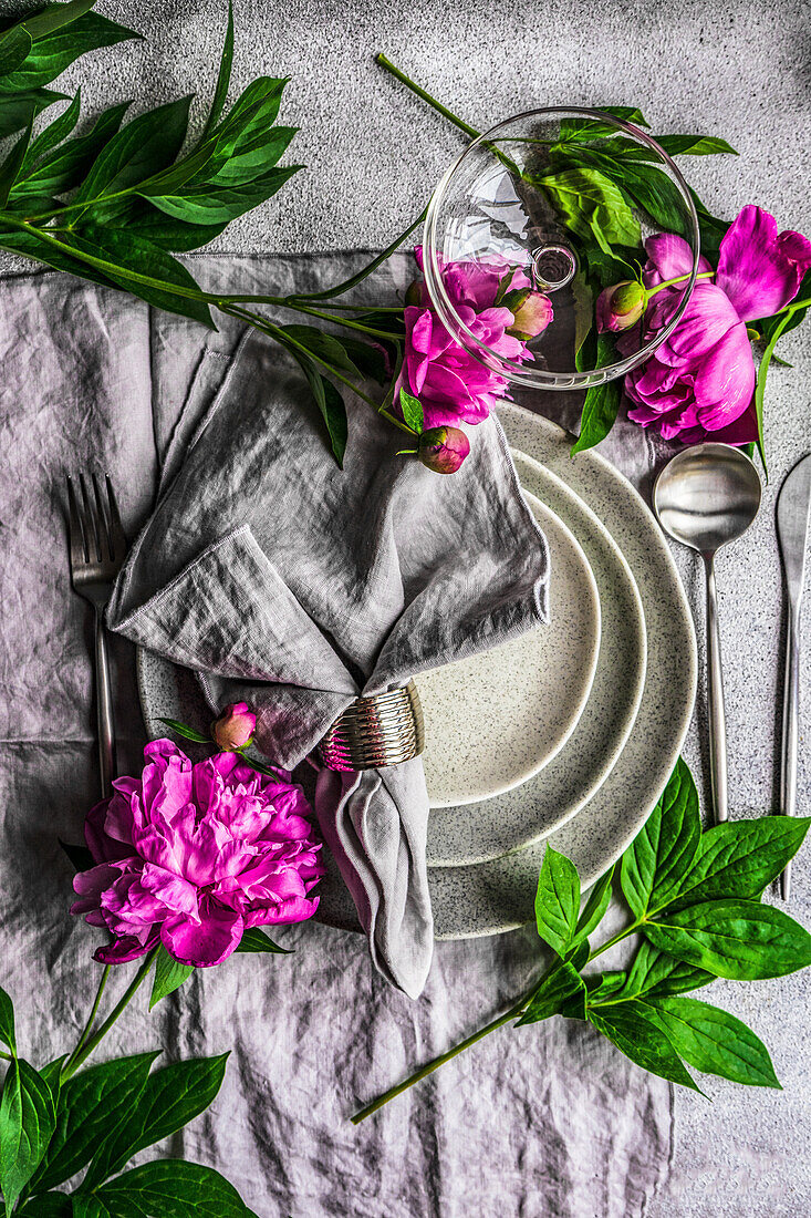 A place setting with a fabric napkin and peonies