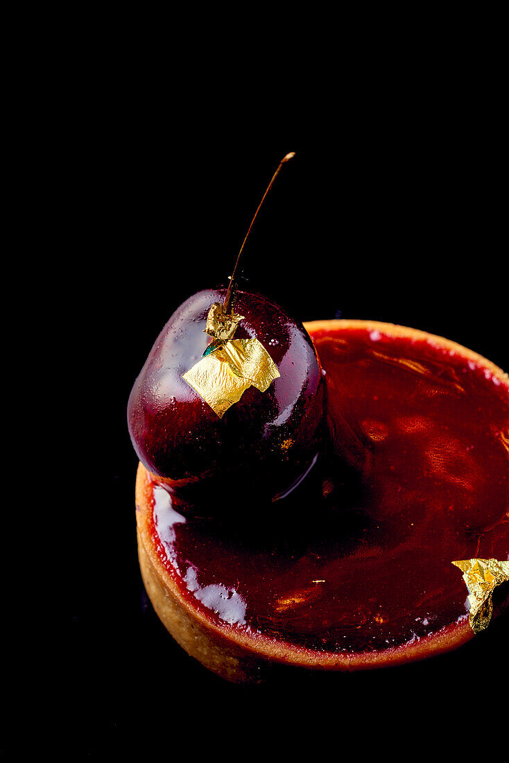 Red wine and cherry tartlet with gold leaf on a black background