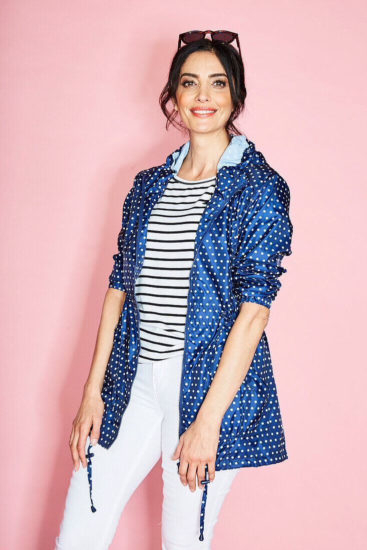 A brunette woman wearing a polk-dot coat, a striped shirt and white trousers