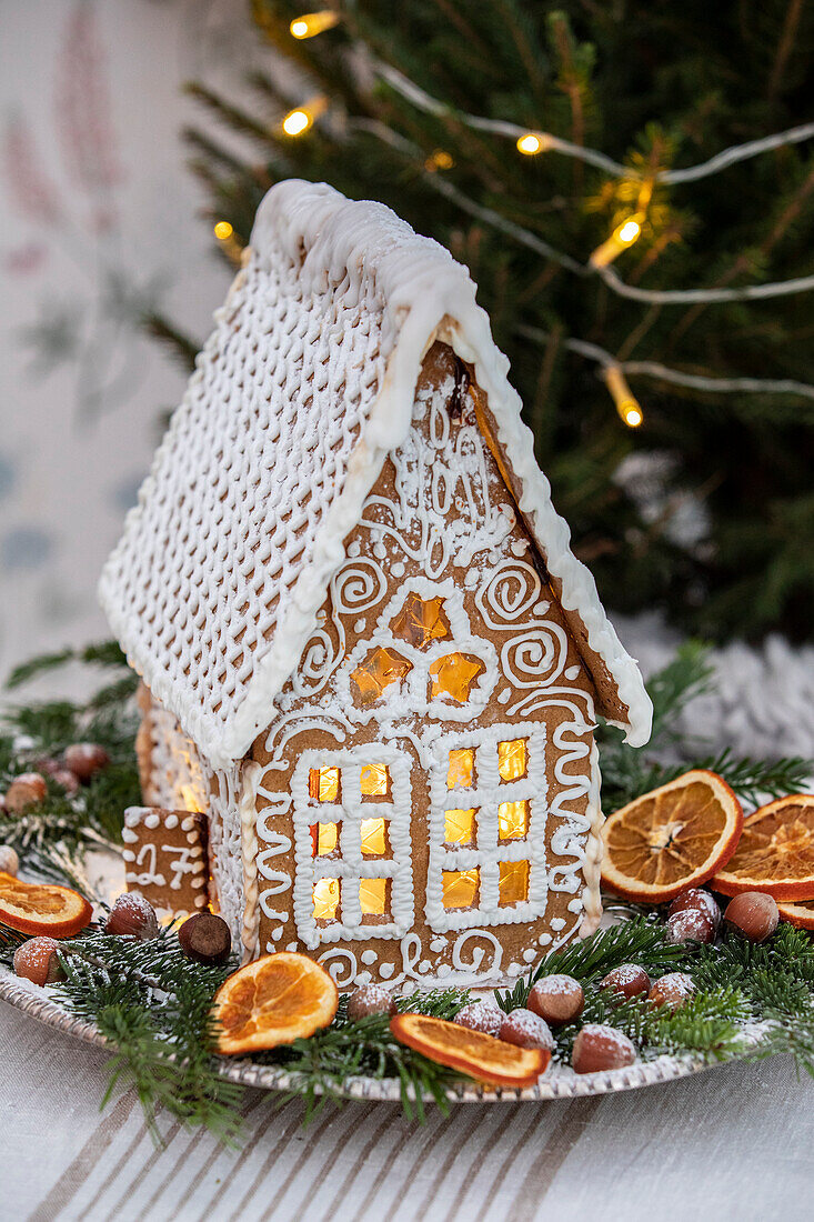 Gingerbread house surrounded by fir branches, candied orange slices and nuts