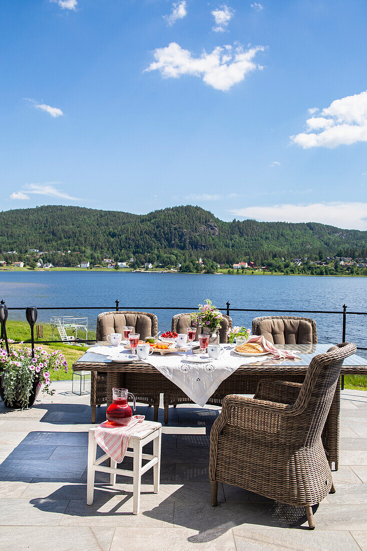 Gedeckter Tisch und Rattansessel auf sonniger Terrasse mit Seeblick