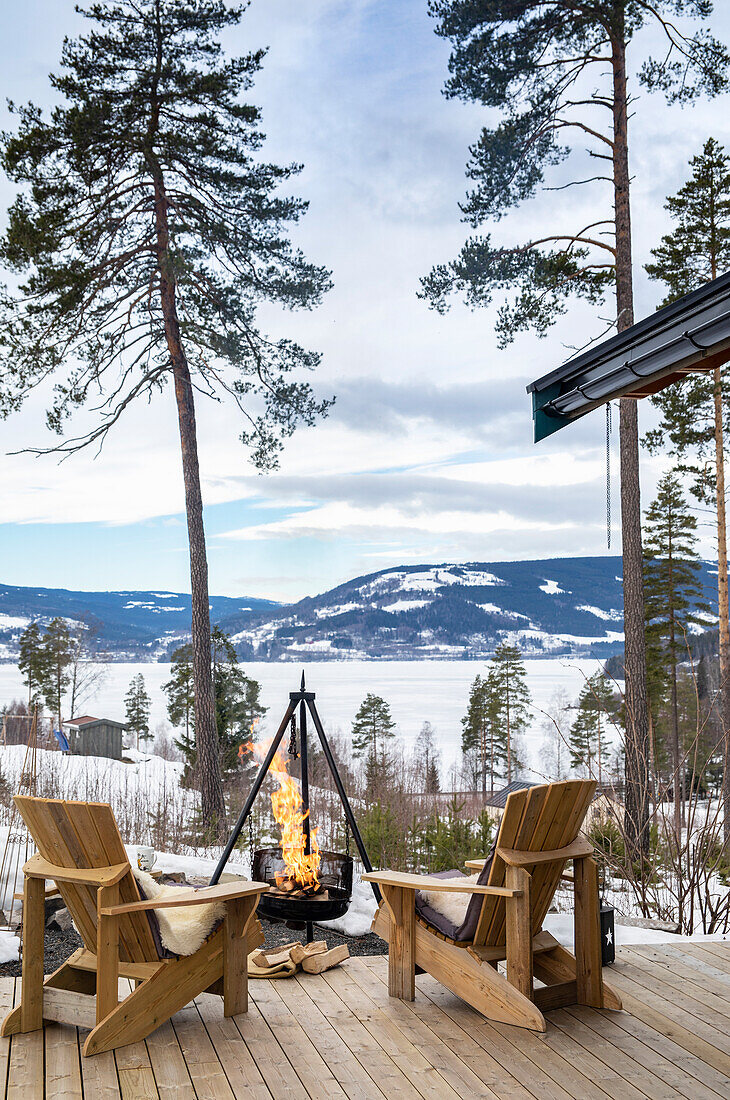Holzstühle und Feuerschale auf Terrasse mit Blick auf schneebedeckte Landschaft, Brøttum in der Region Ringsaker, Innlandet, nähe Lillehammer, Norwegen