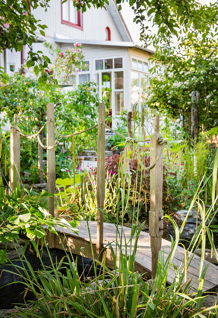 Bogenbrücke aus Holz über Bachlauf im Garten