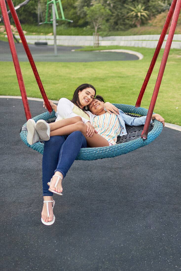 Happy mother and daughter on playground trampoline swing
