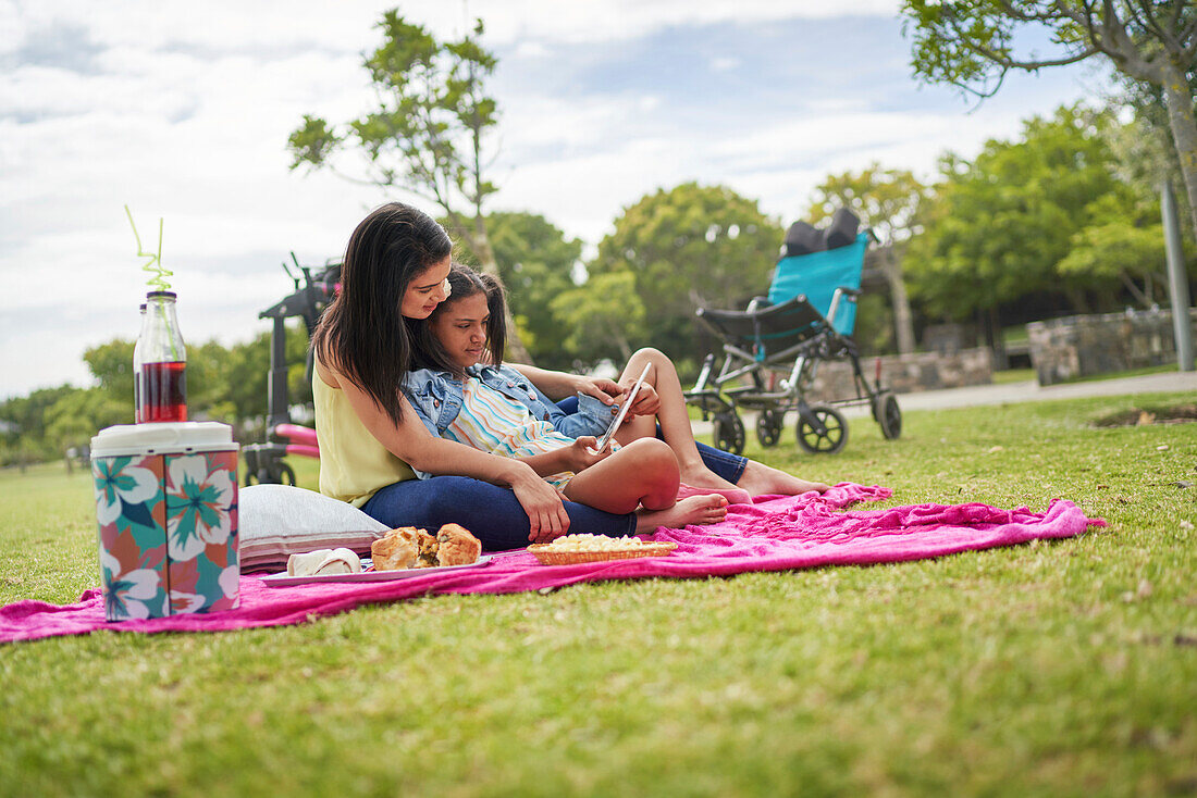 Mum and disabled daughter using tablet on picnic blanket