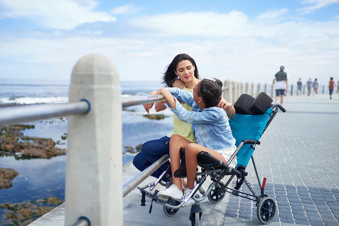 Mum and disabled daughter in pushchair on beach boardwalk