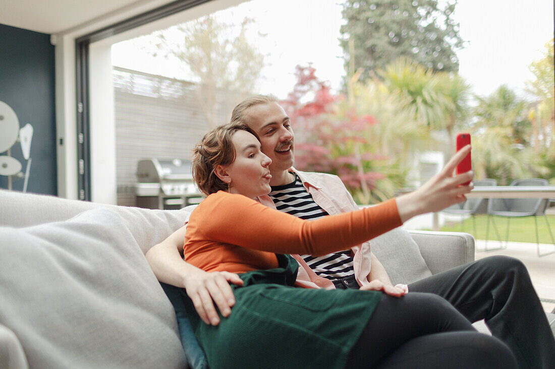 Playful couple taking selfie with smart phone on sofa